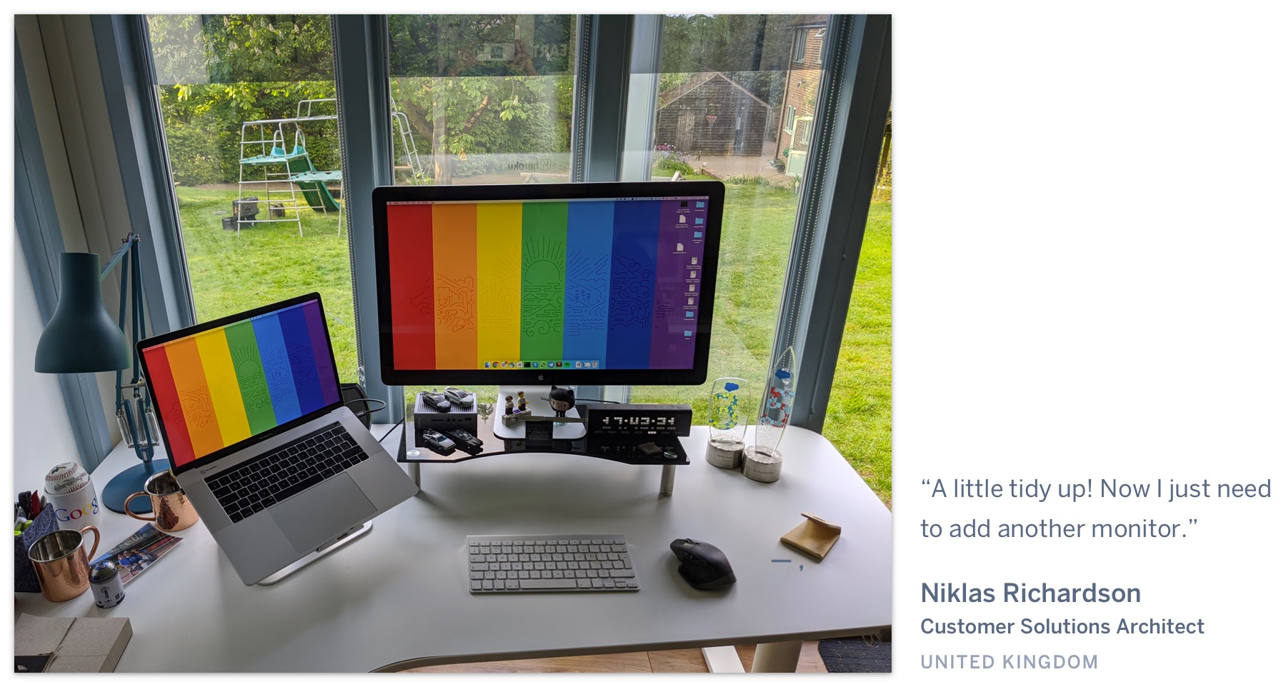 A computer on a desk with a pride wallpaper, in a shed with a view of a grassy backyard. "A little tidy up! Now I just need to add another monitor." Niklas Richardson, Customer Solutions Architect, United Kingdom.